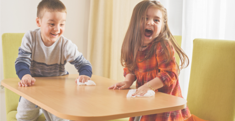 Two children giggling while cleaning an activity table